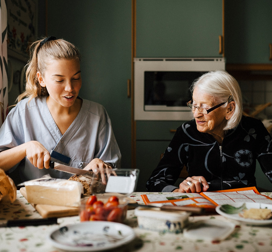 An older woman sits beside a younger woman chatting as she prepares food.