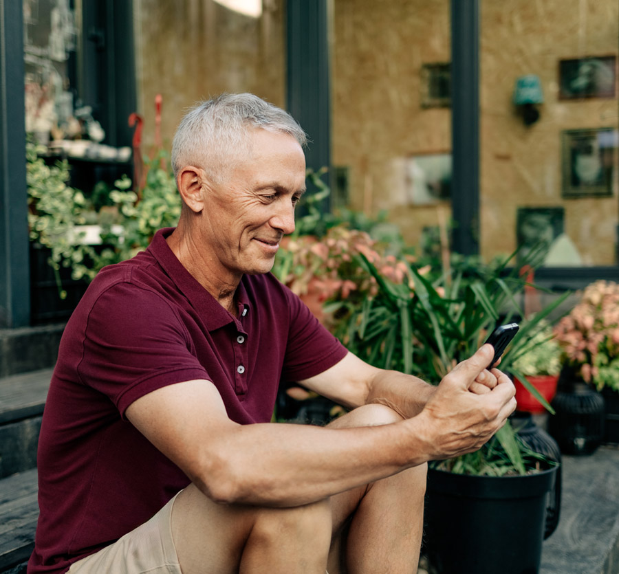 Mature man sitting by plants holding mobile phone