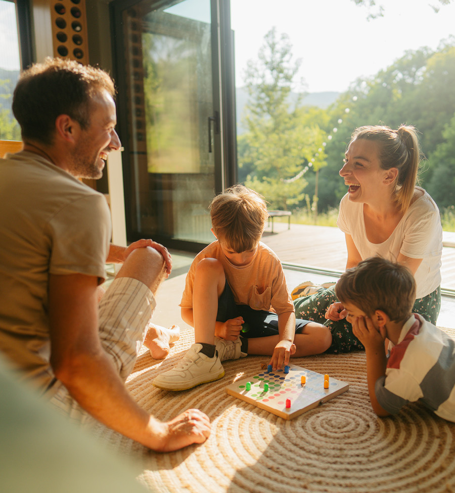 A mother and father play a board game on living room floor with two young boys.