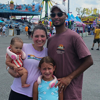 A young mom, dad, daughter, and baby pose for a happy photo at the local county fair.
